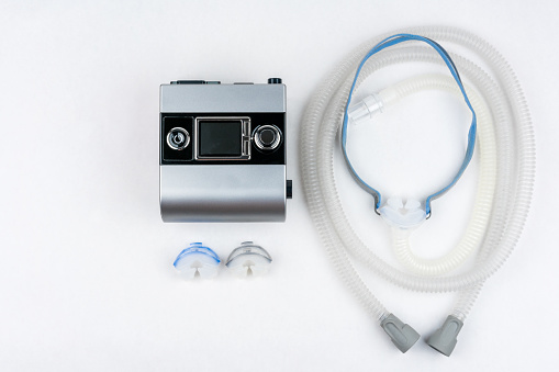 CPAP machine with hose and mask for nose. Treatment for people with sleep apnea, respiratory, or breathing disorder. Studio shot from above on white.
