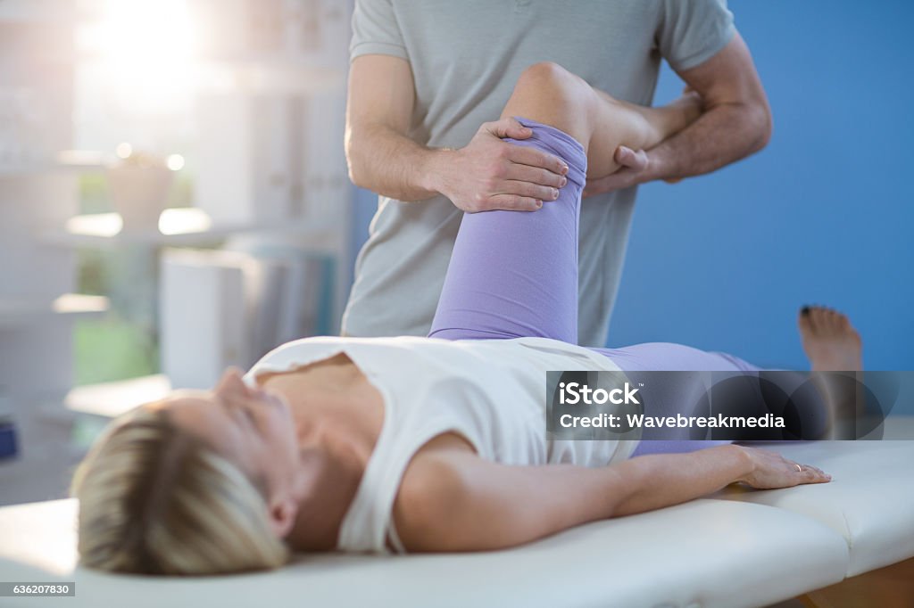 Male physiotherapist giving knee massage to female patient Male physiotherapist giving knee massage to female patient in clinic Massaging Stock Photo