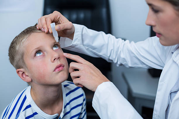 Female optometrist putting eye drop in young patient eyes stock photo