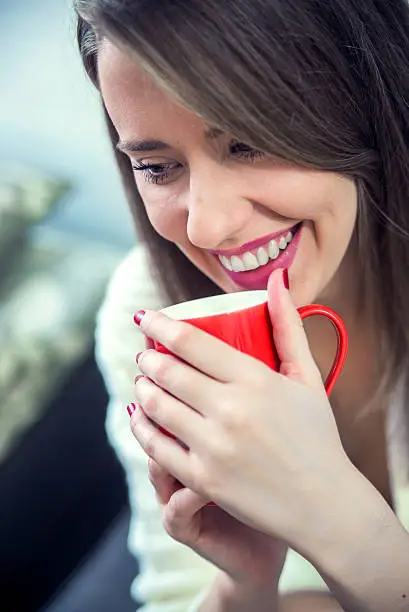 Woman's hand holding a red cup of coffee. With a beautiful winter manicure. Drink, fashion, morning. Woman enjoying a large cup of freshly brewed hot tea as she relaxes on a sofa in the living room