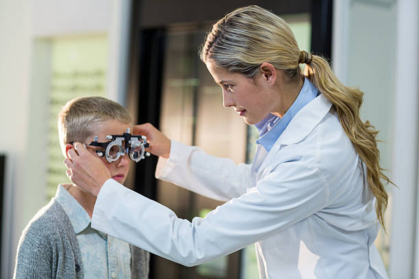 Female optometrist examining young patient with phoropter Female optometrist examining young patient with phoropter in ophthalmology clinic Messbrille stock pictures, royalty-free photos & images