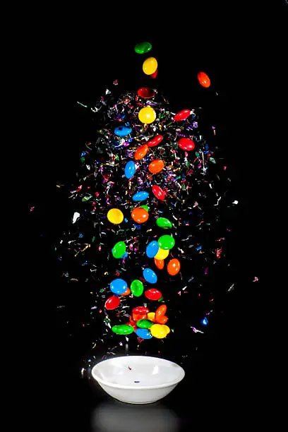 High-speed photo of smarties falling in a white bowl and an explosion of confetti with black background
