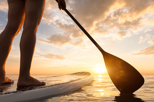 Stand up paddle boarding en el mar tranquilo, piernas de cerca, puesta de sol photo