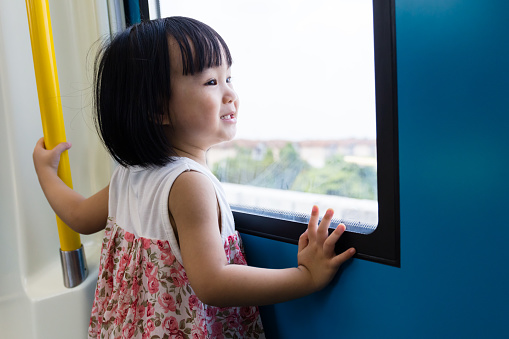 Asian Chinese little girl inside a MRT transit looking far way beside the window.