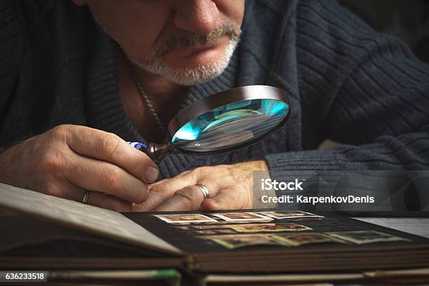 El Hombre Considera El Álbum De Sellos Postales A Través De La Lupa Horizontal Foto de stock y más banco de imágenes de Filatelia