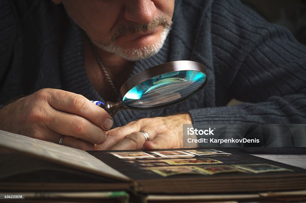 Man considers album of postage stamps trough magnifying glass horizontal Man considers album of  stamps trough the magnifying glass horizontal Stamp Collecting Stock Photo