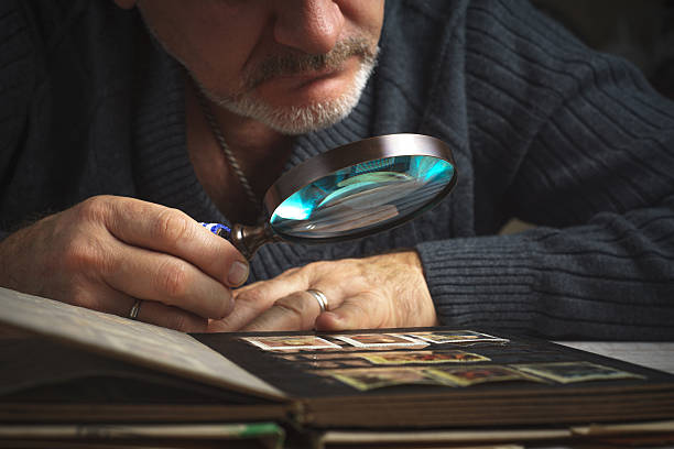 Man considers album of postage stamps trough magnifying glass horizontal stock photo