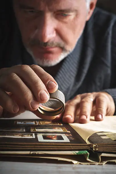 Man considers album of postage stamps trough the magnifying glass vertical