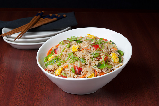 Fried rice with egg and vegetables, onion, bell pepper, carrot, green peas. Prepared and served in a light blue plate, chopsticks.