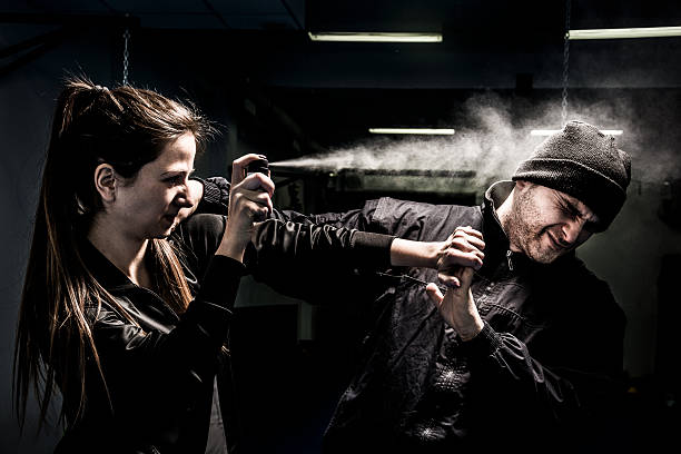 Woman using pepper spray for self defense against attacker The young woman is defending herself from an attacker. Mixed pair demonstrates using of a pepper spray for self defense. The attacker - a young man, wearing a black jacket and knit cap. tear gas stock pictures, royalty-free photos & images