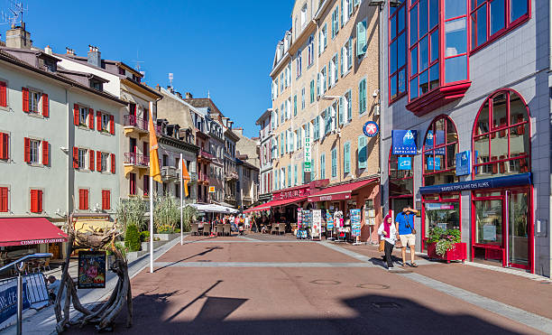 Evian-les-Bains, France. Building facades, with tourists walking Evian-les-Bains, France - July 19, 2016: Building facades in the old town, with tourists walking, and people sitting in an outdoor restaurant. evian les bains stock pictures, royalty-free photos & images
