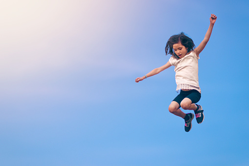 A young girl jumping/bouncing up against a blue sky.