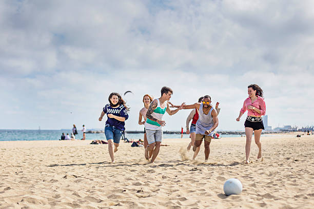 group of friends playing football on the beach - beach football imagens e fotografias de stock