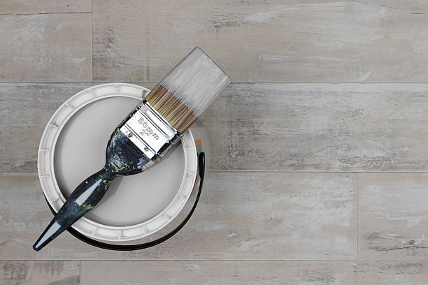 Loaded paintbrush placed across an open can of grey paint