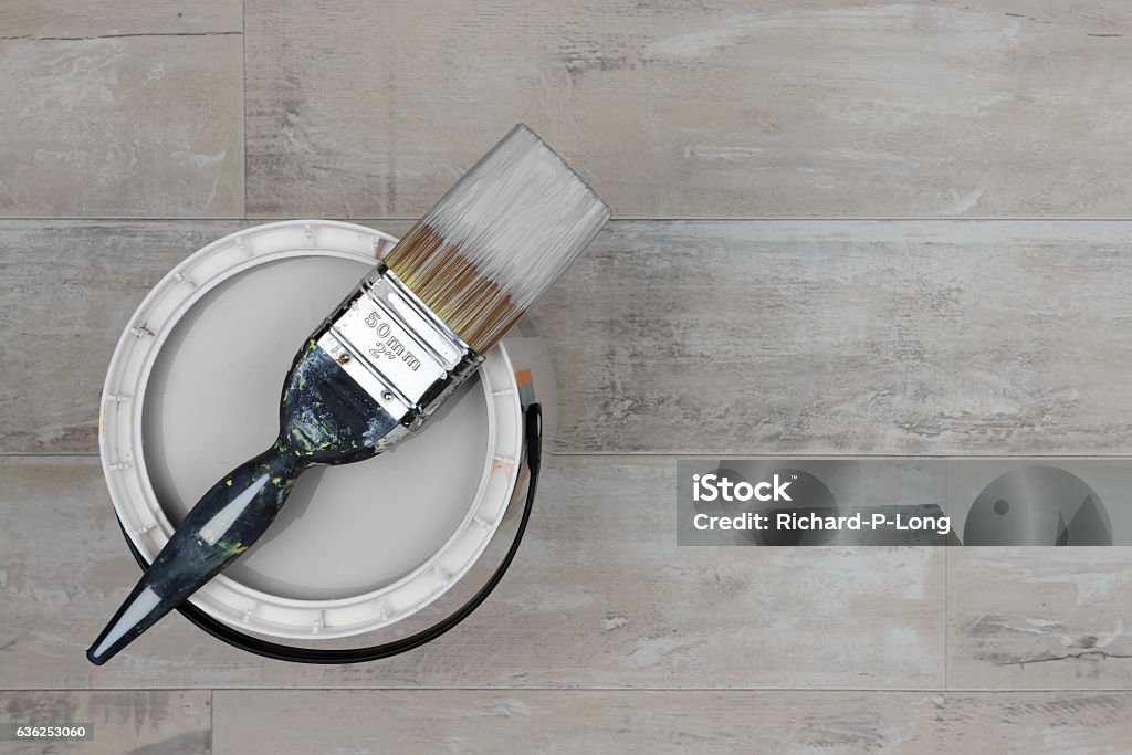 Loaded paintbrush placed across an open can of grey paint Looking down on loaded paintbrush placed across an open can of grey paint stood on a shabby style wood floor Paint Can Stock Photo
