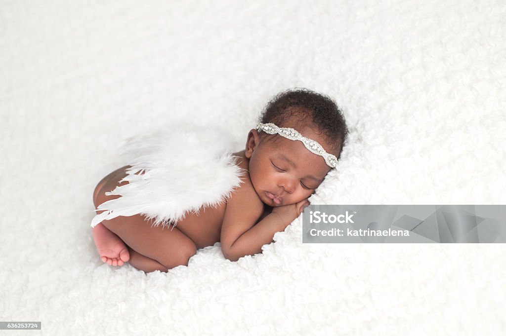 Newborn Baby Girl Wearing Angel Wings Portrait of a one month old, sleeping, newborn, baby girl. She is wearing a rhinestone headband, feather angel wings, and sleeping on a white blanket. Newborn Stock Photo