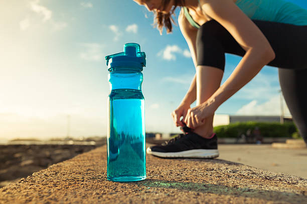 female runner tying her shoes next to bottle of water - shoe tying adult jogging imagens e fotografias de stock