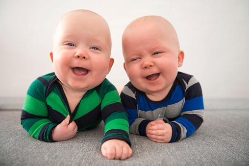 Identical twins lying down on grey mattress