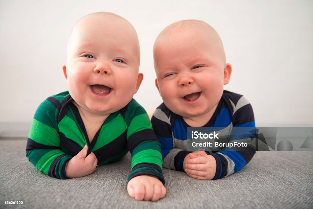 Identical twins laughing Identical twins lying down on grey mattress Baby - Human Age Stock Photo