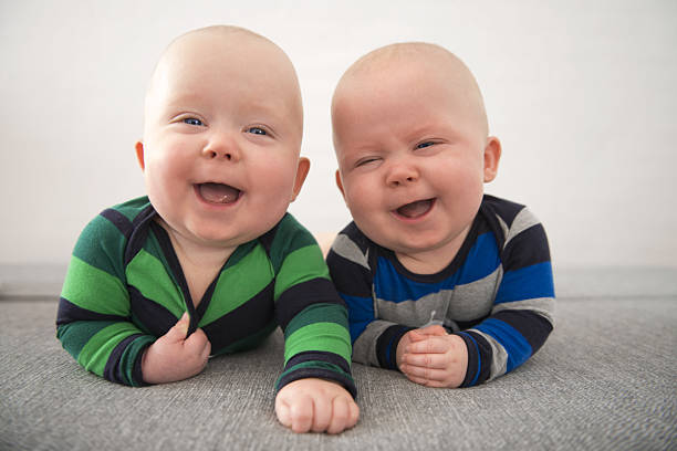 Identical twins laughing Identical twins lying down on grey mattress babies or child stock pictures, royalty-free photos & images