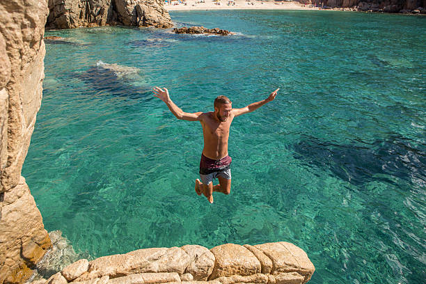 istock Young man jumps off the cliff into the sea 636264446