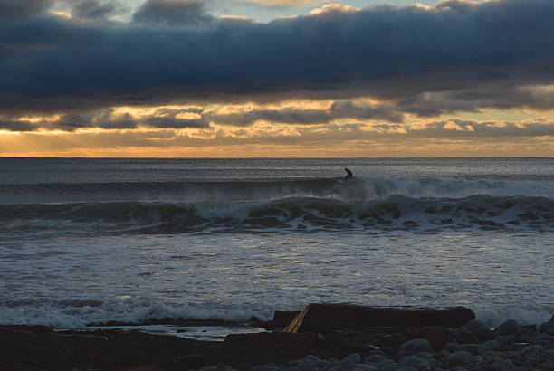 A surfer surfing a cold wave at surnrise in atlantic Canada