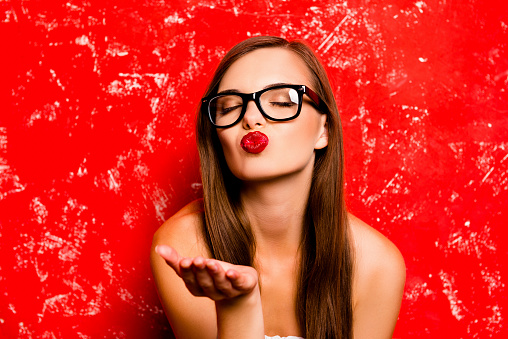 Pretty girl with glasses sending a kiss against the red background