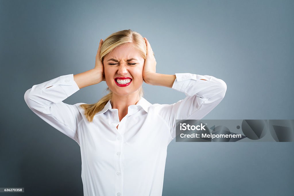 Young woman blocking her ears Young woman blocking her ears on a gray background Fingers in Ears Stock Photo