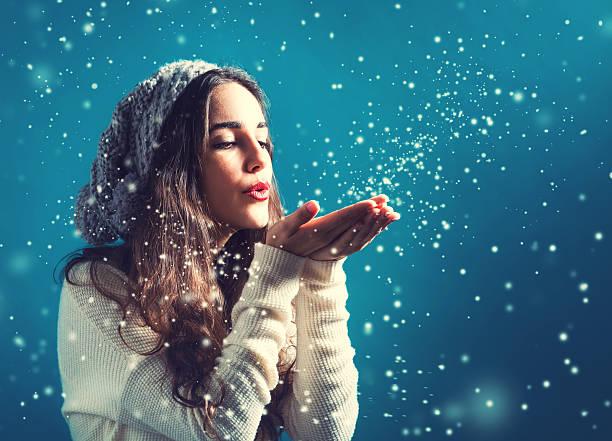 Happy young woman with winter clothes blowing snow