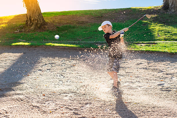 garçon golfeur frappant un bunker de sable - niveau junior photos et images de collection