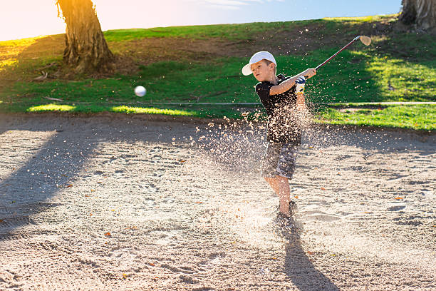 Menino golfista batendo para fora um bunker de areia - foto de acervo