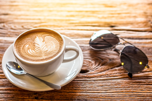 cup of the latte art coffee with spoon and plate on the brown bark beautiful texture background with warm light decorated with sunglasses