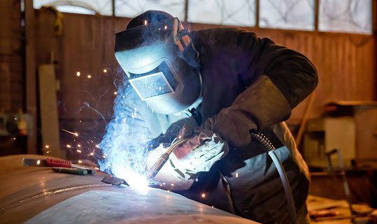 Workers welding metal material. Using protective equipment, fireproof gloves and welding helmet. People working in engineering industrial production.
