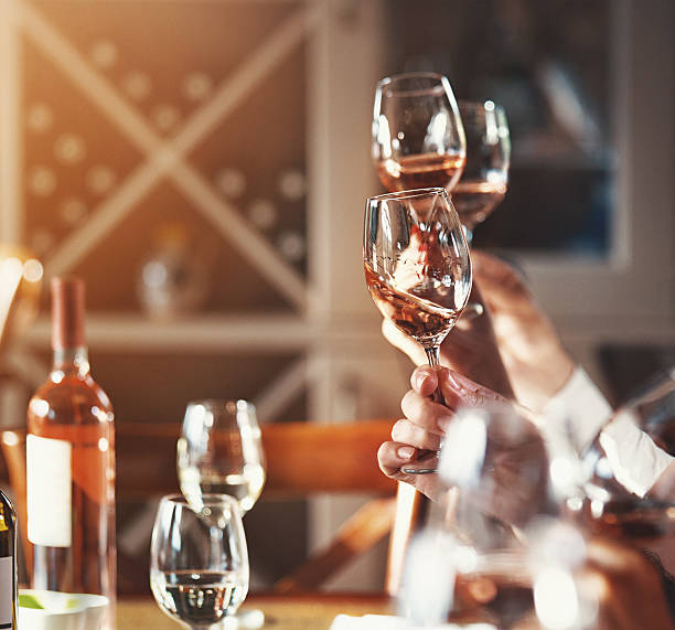 Winetasting event. Closeup side view of group of unrecognizable people performing visual comparison of different sorts of wines. They are gently swirling their glasses to compare color and the alcohol content. The thicker layer of wine on the glass wall the more alcohol there is. winetasting rose wine wineglass elegance stock pictures, royalty-free photos & images