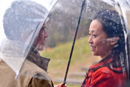 Japanese couple in their 40s is talking in an intimate mood under umbella on a rainy day by Kamo River in Kyoto, Japan.
