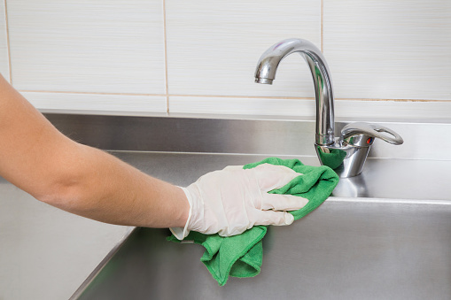 Hand in protective glove with rag cleaning kitchen equipment in the professional kitchen. Stainless steel sink. Early spring cleaning or regular clean up.