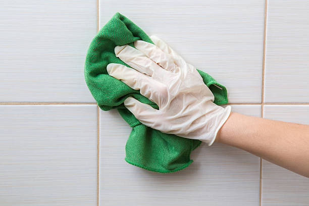 Hand in pink protective glove cleaning tiles with rag.