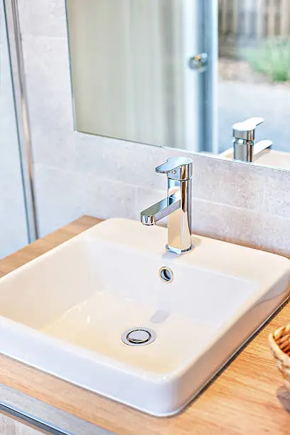 Photo of Modern tap and white sink closeup of a washroom