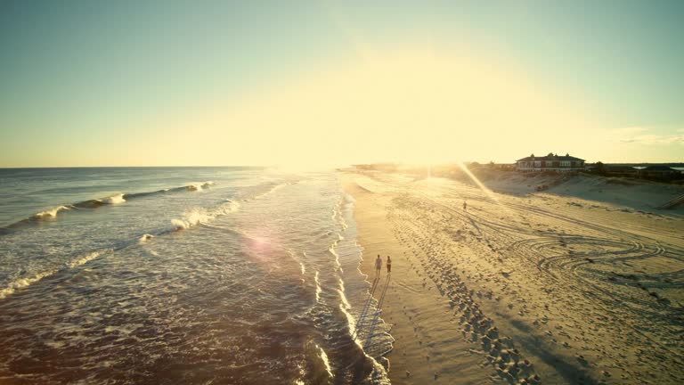 Young man and teenager girl walking together and talking on the beach in Long Island. Aerial footage.