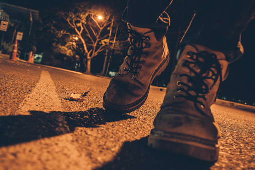 Low Section Of Man Wearing Shoes And Walking On Street At Night