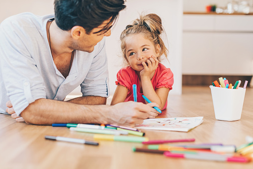 Father and daughter coloring pages on the floor in the living room.