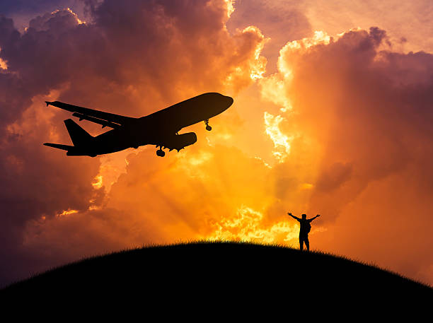 istock silhouette man raised up arms with plane flying in sunset 636313746
