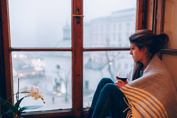 depressed woman sitting near the window - depression women sadness window imagens e fotografias de stock