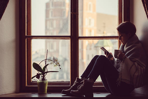 woman on the window texting - stereotypical housewife depression sadness women imagens e fotografias de stock