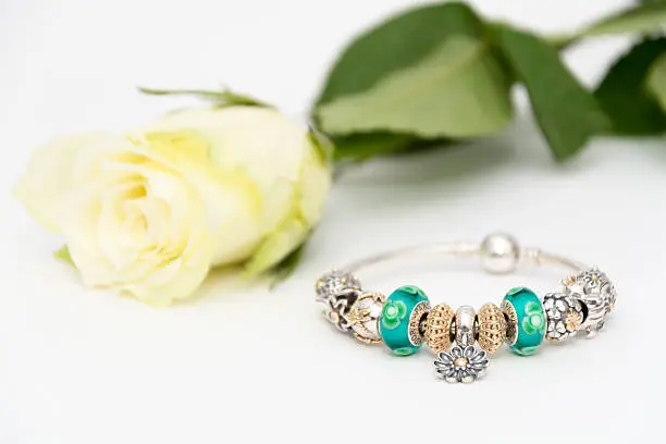 Beautiful Pandora bracelet combined of different charms (beams) on white background next to a beautiful rose.