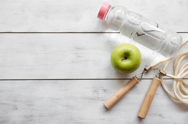 Indicators of healthy lifestyle Green Apple, water bottle and jump rope on white wooden.close up. bottled water on table stock pictures, royalty-free photos & images