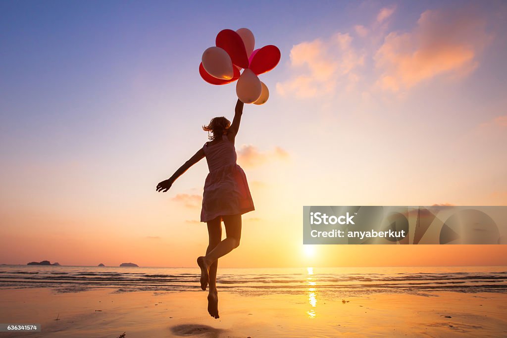 imagination, happy girl flying on multicolored balloons, dreamer imagination, happy girl jumping with multicolored balloons at sunset on the beach, fly, follow your dream Women Stock Photo