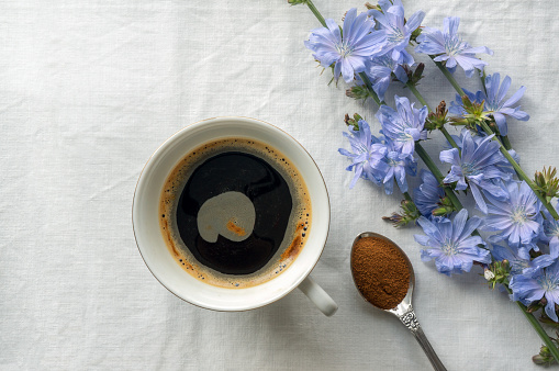 Chicory cup drink and blue flowers on tablecloth. Top view