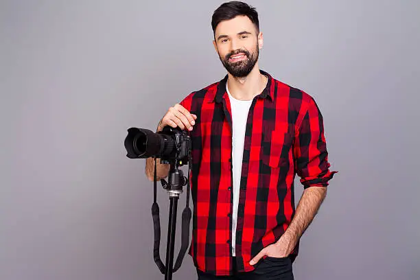 Portrait of handsome young cameraman standing in studio with camera