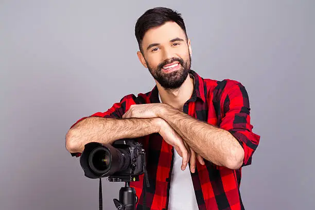 Cheerful happy young man standing with camera in studio